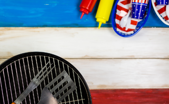 red, white, and blue table with grill surface & utensils in bottom corner, & picnic items on top 