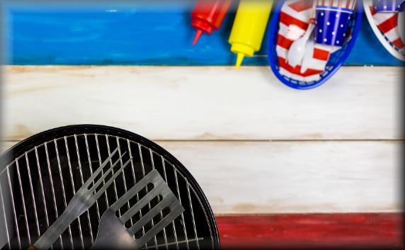 Grill and condiments on red, white, and blue picnic table