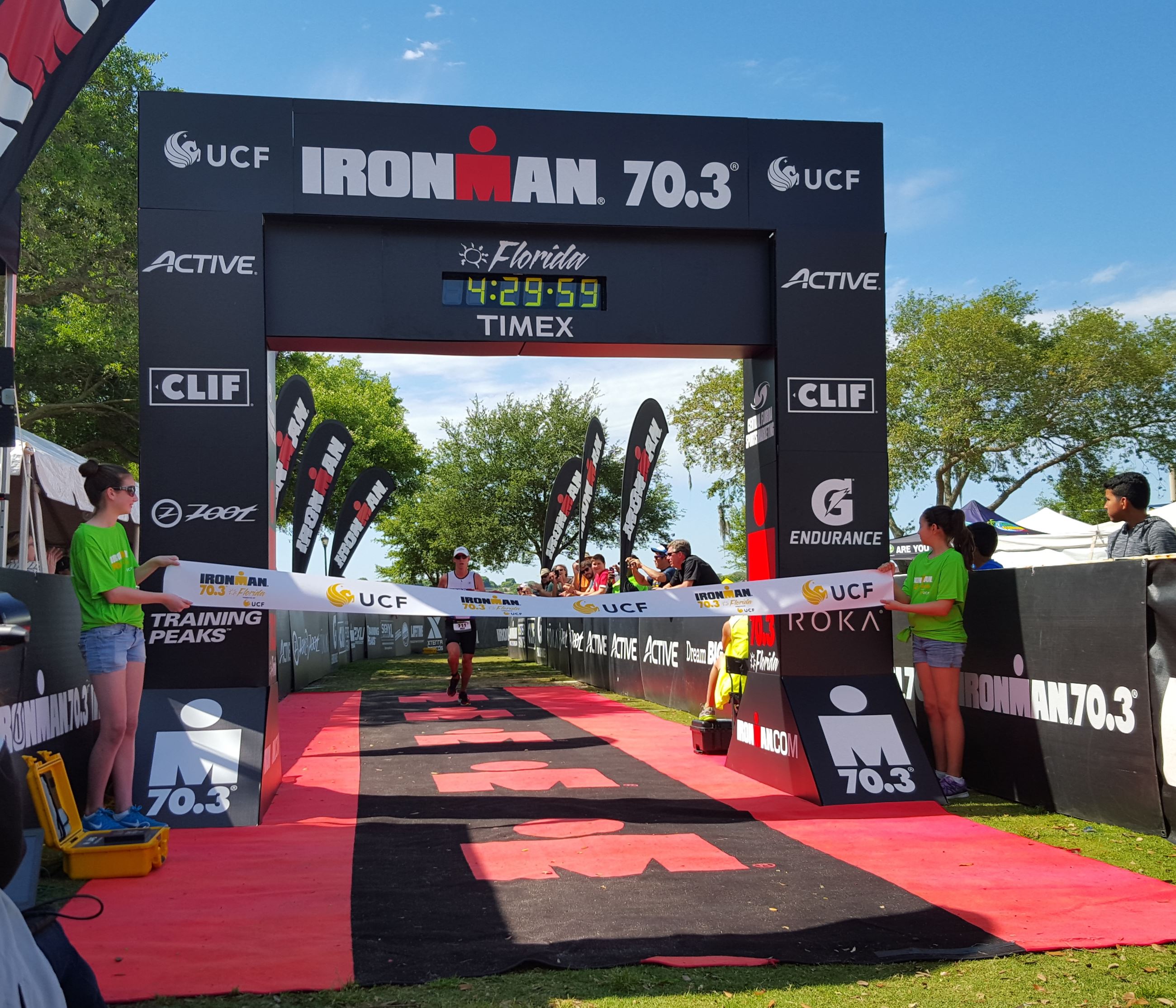2 girls in yellow shirts hold the tape for a man running at a finish line outside